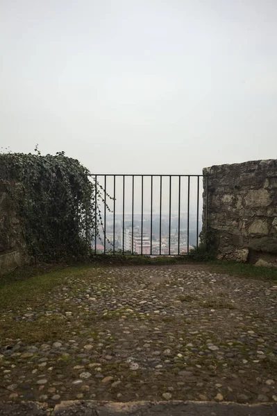 Küçük taş bir duvarın içinde, altında bir şehir, bulutlu ve sisli bir gökyüzünü çerçeveliyor.