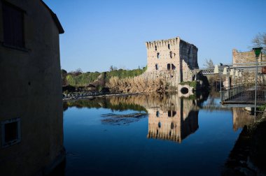 Bir yol köprüsü arasında, içinden geçen ve bir sınır duvarının kalıntıları üzerinde, kışın güneşli bir günde uzaktan görülen yapıyı yansıtan bir nehrin üzerindeki kaleler.