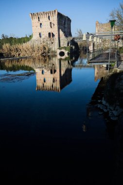 Bir yol köprüsü arasında, içinden geçen ve bir sınır duvarının kalıntıları üzerinde, kışın güneşli bir günde uzaktan görülen yapıyı yansıtan bir nehrin üzerindeki kaleler.