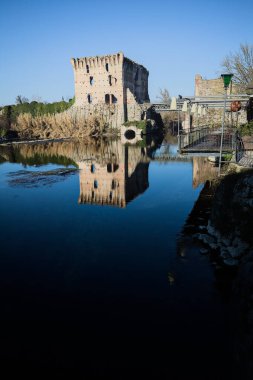 Bir yol köprüsü arasında, içinden geçen ve bir sınır duvarının kalıntıları üzerinde, kışın güneşli bir günde uzaktan görülen yapıyı yansıtan bir nehrin üzerindeki kaleler.