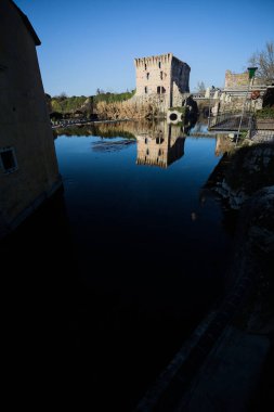 Bir yol köprüsü arasında, içinden geçen ve bir sınır duvarının kalıntıları üzerinde, kışın güneşli bir günde uzaktan görülen yapıyı yansıtan bir nehrin üzerindeki kaleler.