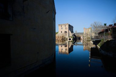 Bir yol köprüsü arasında, içinden geçen ve bir sınır duvarının kalıntıları üzerinde, kışın güneşli bir günde uzaktan görülen yapıyı yansıtan bir nehrin üzerindeki kaleler.