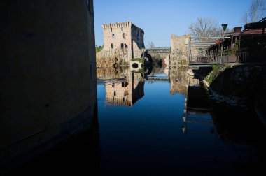 Bir yol köprüsü arasında, içinden geçen ve bir sınır duvarının kalıntıları üzerinde, kışın güneşli bir günde uzaktan görülen yapıyı yansıtan bir nehrin üzerindeki kaleler.