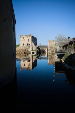 Bir yol köprüsü arasında, içinden geçen ve bir sınır duvarının kalıntıları üzerinde, kışın güneşli bir günde uzaktan görülen yapıyı yansıtan bir nehrin üzerindeki kaleler.