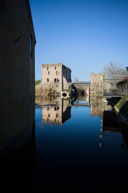 Bir yol köprüsü arasında, içinden geçen ve bir sınır duvarının kalıntıları üzerinde, kışın güneşli bir günde uzaktan görülen yapıyı yansıtan bir nehrin üzerindeki kaleler.