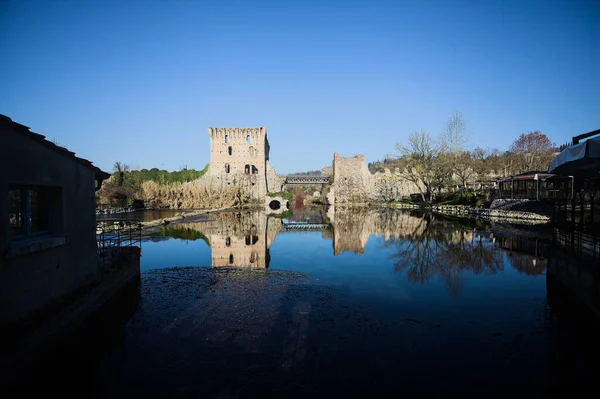 Bir yol köprüsü arasında, içinden geçen ve bir sınır duvarının kalıntıları üzerinde, kışın güneşli bir günde uzaktan görülen yapıyı yansıtan bir nehrin üzerindeki kaleler.