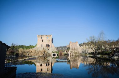 Bir yol köprüsü arasında, içinden geçen ve bir sınır duvarının kalıntıları üzerinde, kışın güneşli bir günde uzaktan görülen yapıyı yansıtan bir nehrin üzerindeki kaleler.