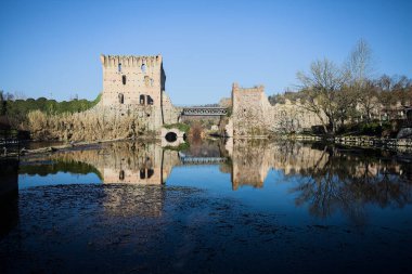 Bir yol köprüsü arasında, içinden geçen ve bir sınır duvarının kalıntıları üzerinde, kışın güneşli bir günde uzaktan görülen yapıyı yansıtan bir nehrin üzerindeki kaleler.