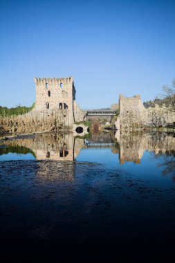 Bir yol köprüsü arasında, içinden geçen ve bir sınır duvarının kalıntıları üzerinde, kışın güneşli bir günde uzaktan görülen yapıyı yansıtan bir nehrin üzerindeki kaleler.