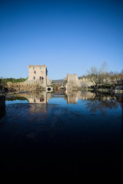 Bir yol köprüsü arasında, içinden geçen ve bir sınır duvarının kalıntıları üzerinde, kışın güneşli bir günde uzaktan görülen yapıyı yansıtan bir nehrin üzerindeki kaleler.