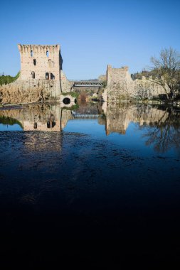 Bir yol köprüsü arasında, içinden geçen ve bir sınır duvarının kalıntıları üzerinde, kışın güneşli bir günde uzaktan görülen yapıyı yansıtan bir nehrin üzerindeki kaleler.