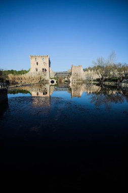 Bir yol köprüsü arasında, içinden geçen ve bir sınır duvarının kalıntıları üzerinde, kışın güneşli bir günde uzaktan görülen yapıyı yansıtan bir nehrin üzerindeki kaleler.