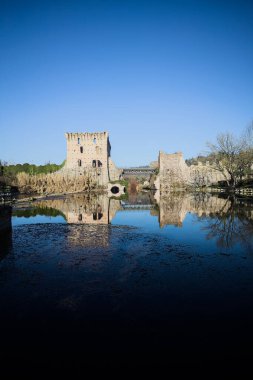 Bir yol köprüsü arasında, içinden geçen ve bir sınır duvarının kalıntıları üzerinde, kışın güneşli bir günde uzaktan görülen yapıyı yansıtan bir nehrin üzerindeki kaleler.