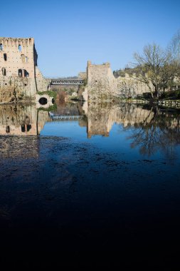 Bir yol köprüsü arasında, içinden geçen ve bir sınır duvarının kalıntıları üzerinde, kışın güneşli bir günde uzaktan görülen yapıyı yansıtan bir nehrin üzerindeki kaleler.