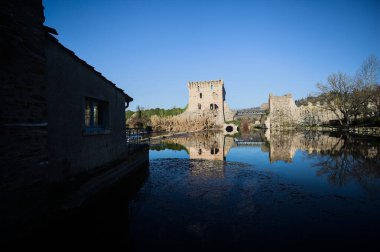 Bir yol köprüsü arasında, içinden geçen ve bir sınır duvarının kalıntıları üzerinde, kışın güneşli bir günde uzaktan görülen yapıyı yansıtan bir nehrin üzerindeki kaleler.