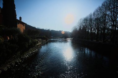 İtalya 'nın kırsal kesiminde bir köyün yanından akan nehir. Evleri, gök mavisi korkulukları, sokak lambaları ve kıyılarında çıplak kavak olan terası olan, güneşli bir günde görünen ve güneş tarafından aydınlatılan bir köy.