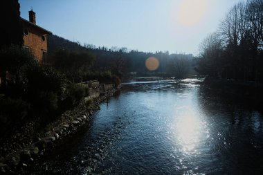 İtalya 'nın kırsal kesiminde bir köyün yanından akan nehir. Evleri, gök mavisi korkulukları, sokak lambaları ve kıyılarında çıplak kavak olan terası olan, güneşli bir günde görünen ve güneş tarafından aydınlatılan bir köy.