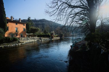 İtalya 'nın kırsal kesiminde bir köyün yanından akan nehir. Evleri, gök mavisi korkulukları, sokak lambaları ve kıyılarında çıplak kavak olan terası olan, güneşli bir günde görünen ve güneş tarafından aydınlatılan bir köy.