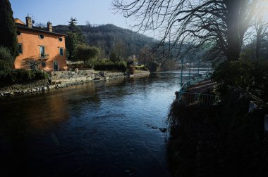 İtalya 'nın kırsal kesiminde bir köyün yanından akan nehir. Evleri, gök mavisi korkulukları, sokak lambaları ve kıyılarında çıplak kavak olan terası olan, güneşli bir günde görünen ve güneş tarafından aydınlatılan bir köy.