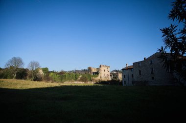 Çimlerle çevrili gölgeli evler çimlerin büyük bir kısmını kaplayan bir gölge ve güneşli bir günde görülen arka planda bir kalenin kalıntıları.