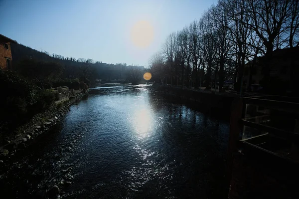 İtalya 'nın kırsal kesiminde bir köyün yanından akan nehir. Evleri, gök mavisi korkulukları, sokak lambaları ve kıyılarında çıplak kavak olan terası olan, güneşli bir günde görünen ve güneş tarafından aydınlatılan bir köy.