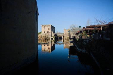 Bir yol köprüsü arasında, içinden geçen ve bir sınır duvarının kalıntıları üzerinde, kışın güneşli bir günde uzaktan görülen yapıyı yansıtan bir nehrin üzerindeki kaleler.