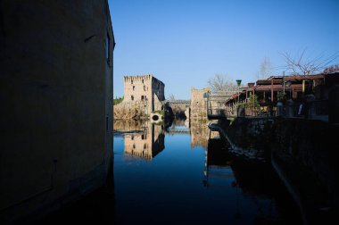Bir yol köprüsü arasında, içinden geçen ve bir sınır duvarının kalıntıları üzerinde, kışın güneşli bir günde uzaktan görülen yapıyı yansıtan bir nehrin üzerindeki kaleler.