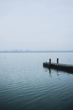 Bir gölde uzanan ahşap demirleme direkleriyle rıhtım, bulutlu ve sisli bir günde, karşı kıyıda, İtalya kırsalında