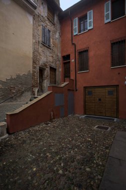 Bulutlu bir günde, iki binanın köşesindeki bir İtalyan kasabasının ara sokağında, cepheye açılan bir kapıya çıkan merdiven.