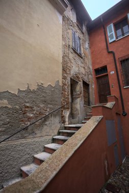 Bulutlu bir günde, iki binanın köşesindeki bir İtalyan kasabasının ara sokağında, cepheye açılan bir kapıya çıkan merdiven.