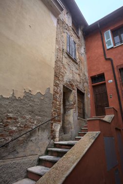 Bulutlu bir günde, iki binanın köşesindeki bir İtalyan kasabasının ara sokağında, cepheye açılan bir kapıya çıkan merdiven.