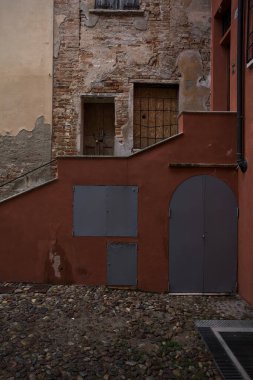 Bulutlu bir günde, iki binanın köşesindeki bir İtalyan kasabasının ara sokağında, cepheye açılan bir kapıya çıkan merdiven.