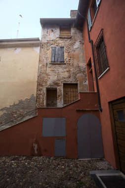 Bulutlu bir günde, iki binanın köşesindeki bir İtalyan kasabasının ara sokağında, cepheye açılan bir kapıya çıkan merdiven.