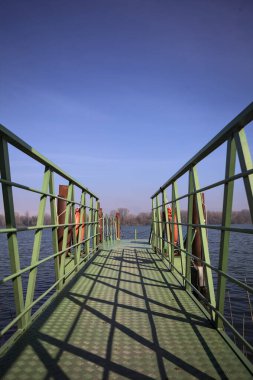 Bir rıhtımın Jetty 'si, bir gölün üzerine uzanan, ucunda demirleme direkleriyle, ve uzakta karşı kıyıda, güneşli bir kış gününde görülen