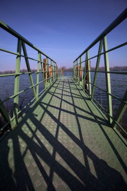 Bir rıhtımın Jetty 'si, bir gölün üzerine uzanan, ucunda demirleme direkleriyle, ve uzakta karşı kıyıda, güneşli bir kış gününde görülen