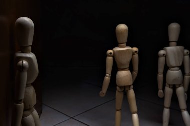 Tahta manken duvara yaslanmış, diğer ahşap mankenlerle birlikte caddeden geçerken izliyormuş gibi yapıyor.