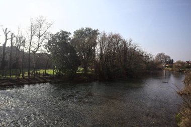 Nehir, İtalya 'nın kırsal kesimindeki bir köyün yanından geçiyor. Nehir kıyısında, güneşli bir günde parkın yanında merdiven kayıyor.