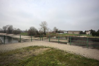 Teras, ağaçlar arasındaki sıra sıra saptırıcı bir kanal üzerinde demiryolu ile çevrili ve İtalya kırsalında bulutlu bir günde balyalarla kaplı bir ahır var.