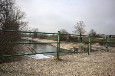 Teras, ağaçlar arasındaki sıra sıra saptırıcı bir kanal üzerinde demiryolu ile çevrili ve İtalya kırsalında bulutlu bir günde balyalarla kaplı bir ahır var.