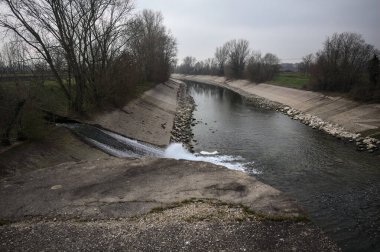 İtalya 'nın kırsal kesimlerinde bulutlu bir günde kıyılarında sıra sıra ağaçlarla oyalanan saptırıcı bir kanal.