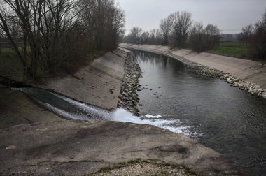 İtalya 'nın kırsal kesimlerinde bulutlu bir günde kıyılarında sıra sıra ağaçlarla oyalanan saptırıcı bir kanal.