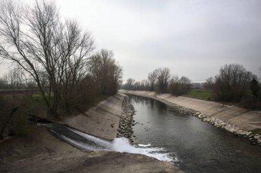 İtalya 'nın kırsal kesimlerinde bulutlu bir günde kıyılarında sıra sıra ağaçlarla oyalanan saptırıcı bir kanal.