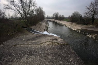 İtalya 'nın kırsal kesimlerinde bulutlu bir günde kıyılarında sıra sıra ağaçlarla oyalanan saptırıcı bir kanal.