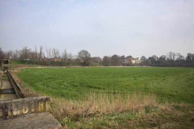 Ağaçlarla çevrili bir toprak seti ve beton sulama kanalı ile çevrili, her taraftan, yukarıdan bakıldığında, İtalya kırsalında bulutlu bir günde