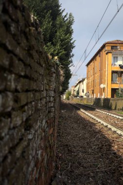 İtalya kırsalında güneşli bir günde yolun kenarındaki bir binanın yanından geçen tren yolu.