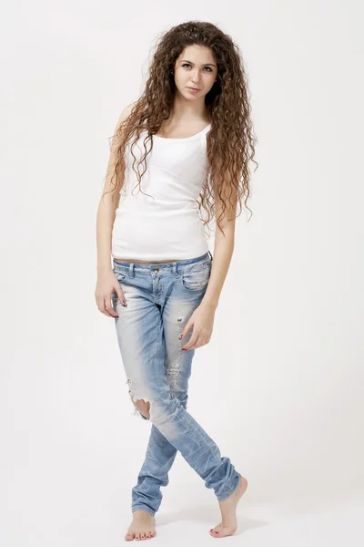 Krásná dívka s dlouhými kudrnatými vlasy nosí bílý top a roztrhané džíny — Stock fotografie