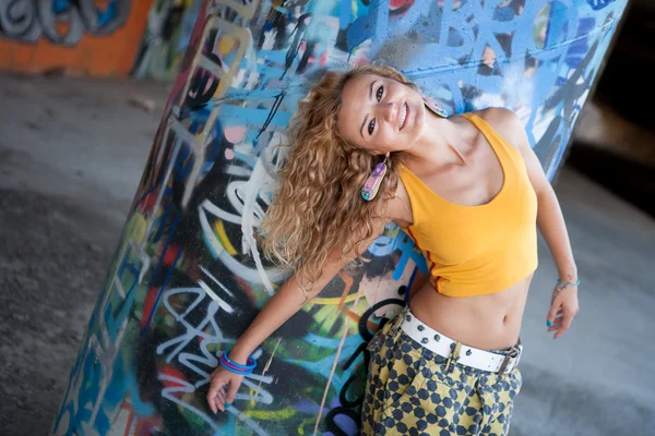Happy hip teenage blonde girl standing by graffiti wall — Stock Photo, Image