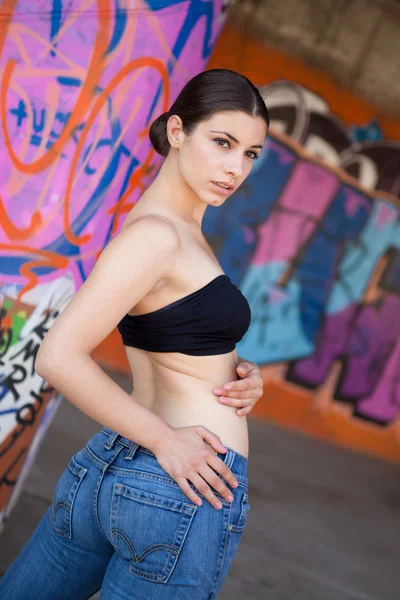 Beautiful girl with black top and jeans in front of graffiti wall — Stock Photo, Image