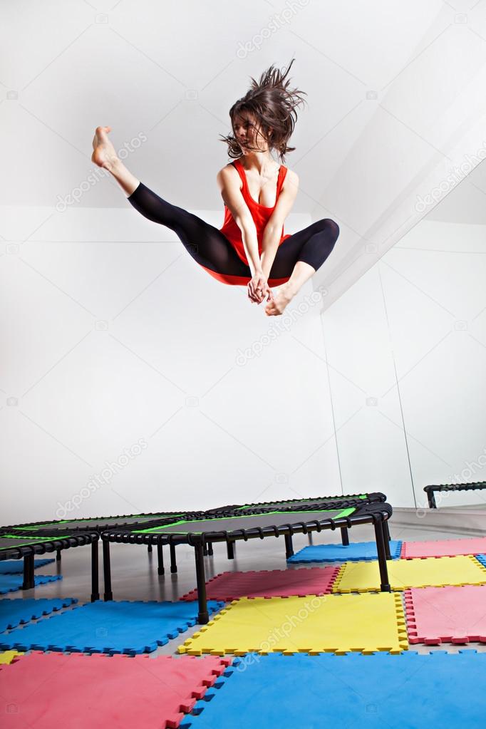 Jumping brunette woman on a trampoline. Wearing red top