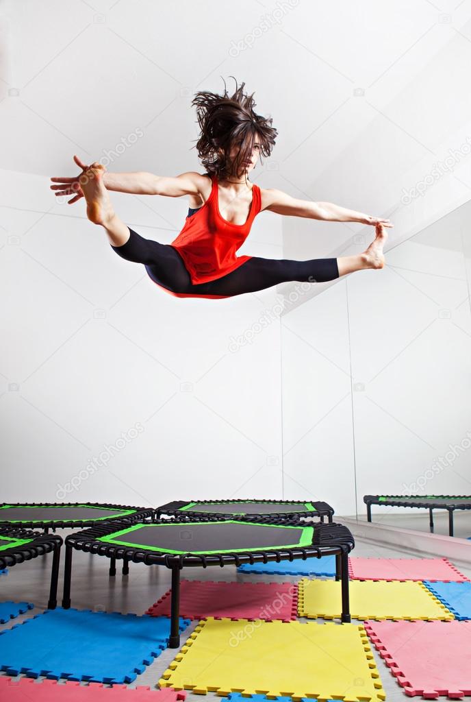 Jumping brunette woman on a trampoline. Wearing red top